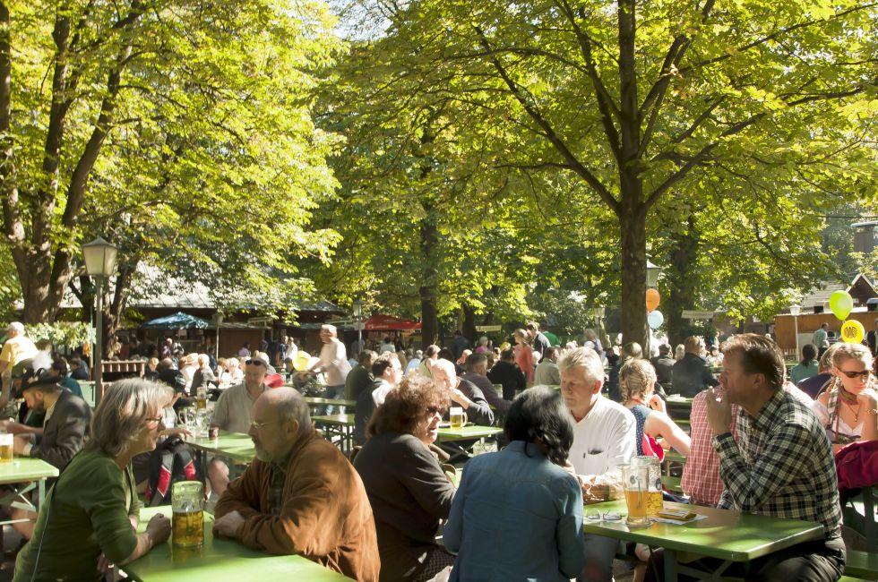 People relax outdoor on a beautiful October day, sitting in the sun, drinking beer and eating Bavarian traditional food in one of the many open air seasonal restaurant (Biergarten) of the Englischer Garten in Munich.