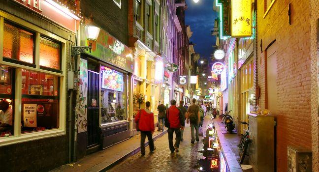 Bars and coffee shops on the street full of tourists at night in famous Red Light District in Amsterdam, Netherlan ds.