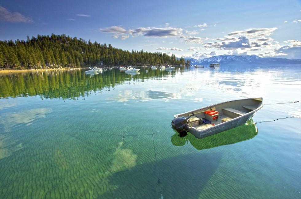 My lonely little fishing  boat setting on the Calm clear water in lake Tahoe, with Trees and Mountains in the background; 