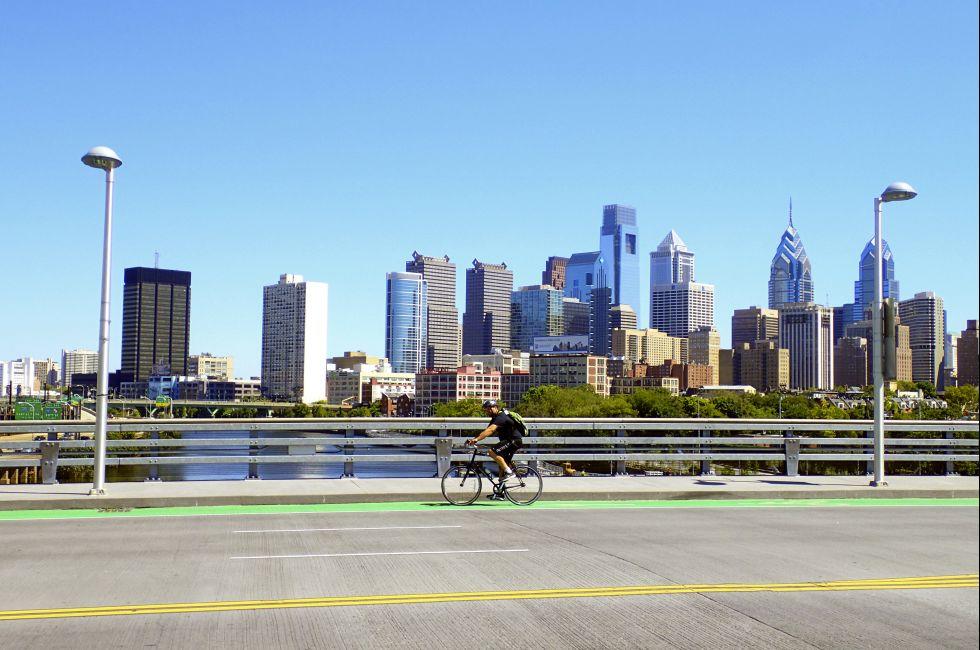 Philadelphia, PA, USA – August 28, 2014: Bicyclist on the South Street Bridge with the Philadelphia Skyline behind him.