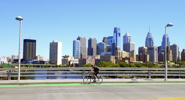 Philadelphia, PA, USA – August 28, 2014: Bicyclist on the South Street Bridge with the Philadelphia Skyline behind him.