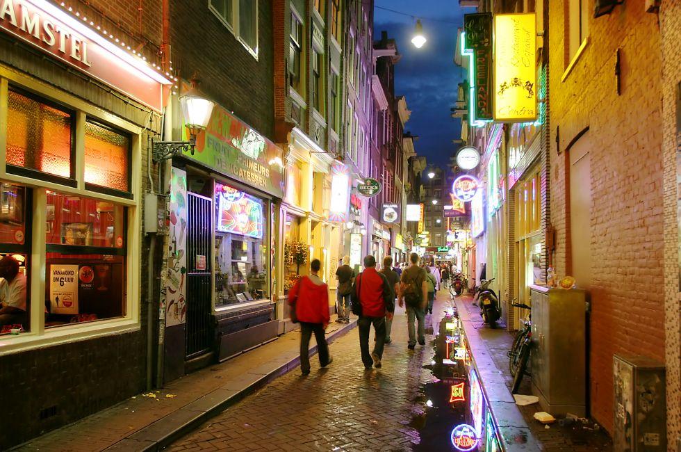 Bars and coffee shops on the street full of tourists at night in famous Red Light District in Amsterdam, Netherlan ds.