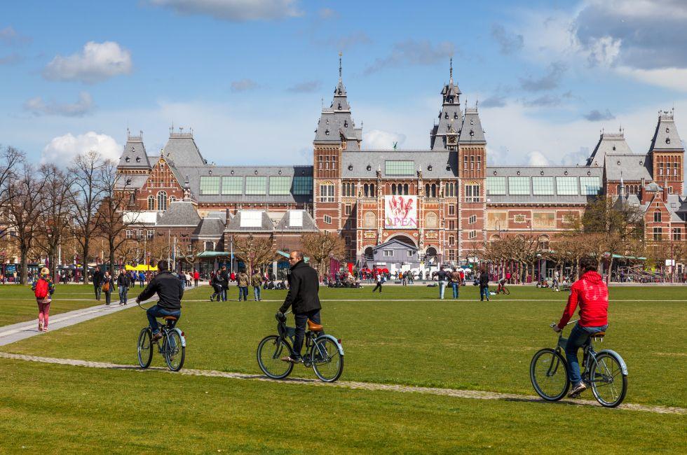 Amsterdam, Netherlands- April 22, 2012: Three men riding their bicycles on a green yard in front of The New Rijksmuseum in Amsterdam.
