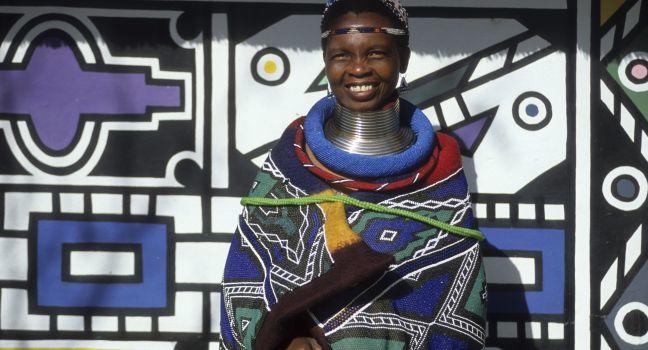 Neck-stretching brass coils announce marrigage as do a beaded jocolo wedding apron that mirrors the primary colors of the decorations hand painted by the mguni-speaking Ndebele.  Bronkhorstspruit, South Africa