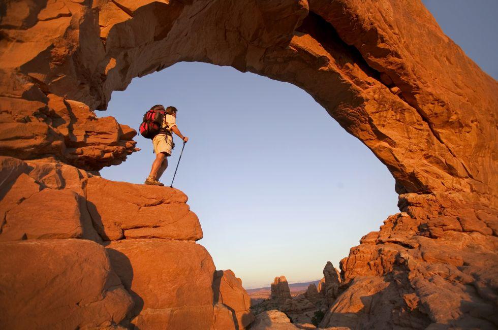 Backpacker standing under magnificent arch in Arches National Park 