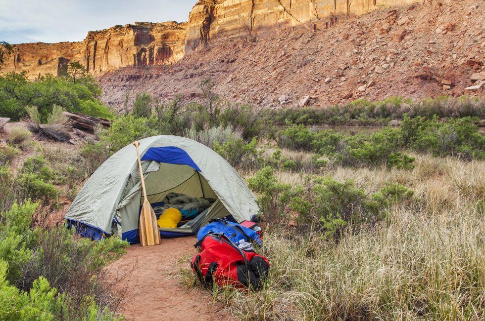 sunrise over river camping in Canyonlands National Park- a tent with canoe paddle and waterproof bags on the shore of Green River