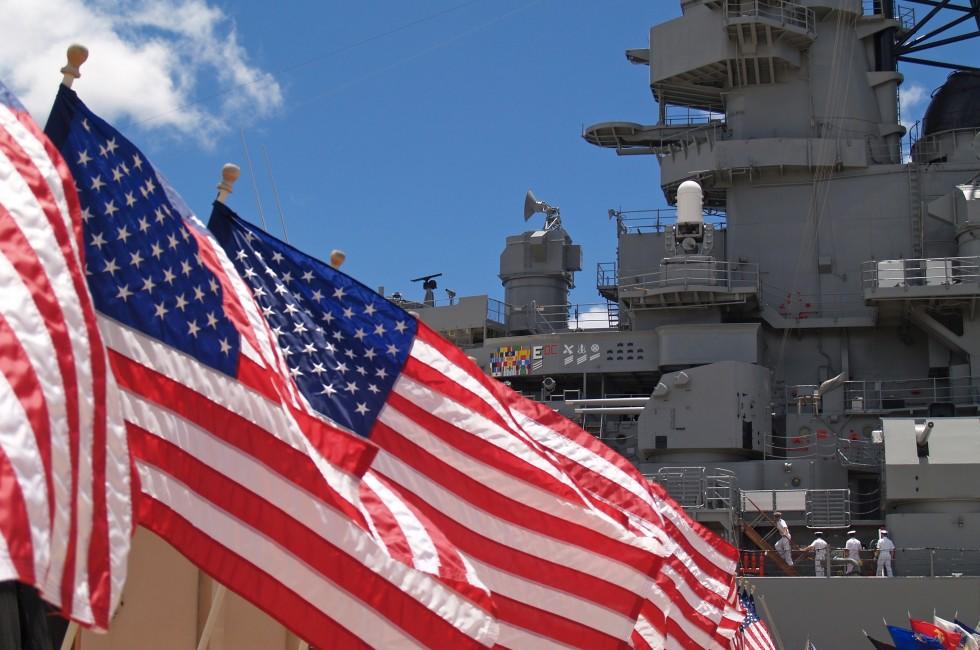 US flags flying beside the Battleship Missouri in Pearl Harbor, Honolulu, Oahu, Hawaii with 4 sailors walking on deck.