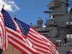 US flags flying beside the Battleship Missouri in Pearl Harbor, Honolulu, Oahu, Hawaii with 4 sailors walking on deck.