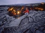 A volcanologist enters a glowing methane gas death zone where slow moving pahoehoe lava speads across the landscape and heads to the Pacific, exploding trees in its path. Hawaii Volcanos National Park