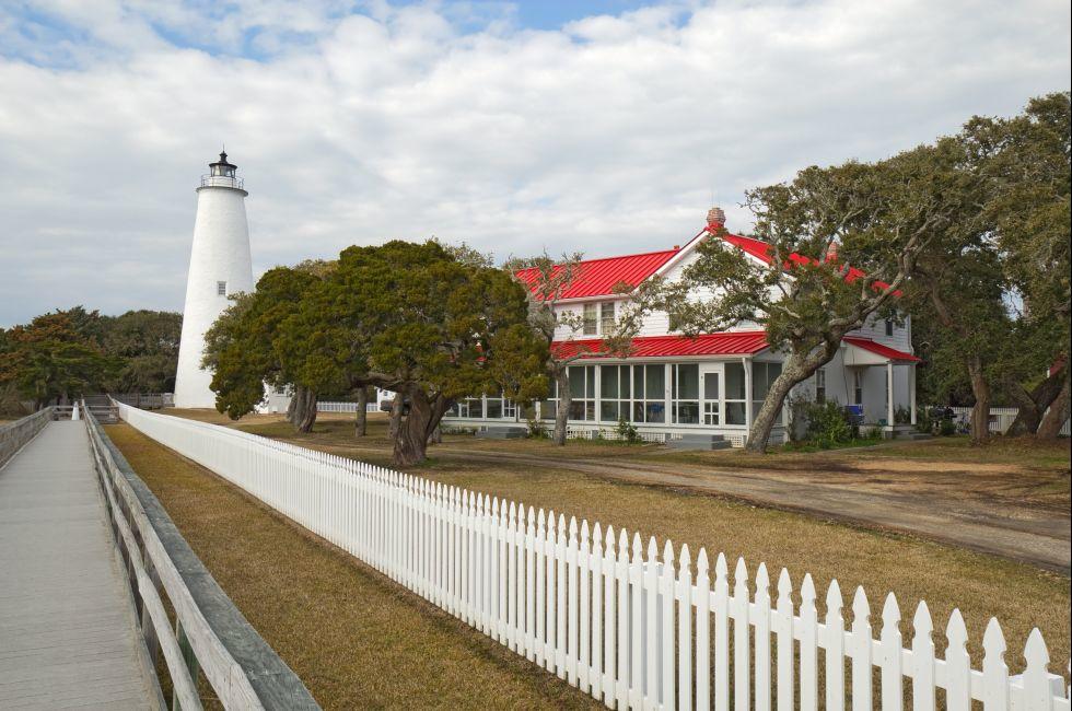 White picket fence and walkway lead past the red-roofed keepers quarters towards the tower of the Ocracoke Island lighthouse on the outer banks of North Carolina