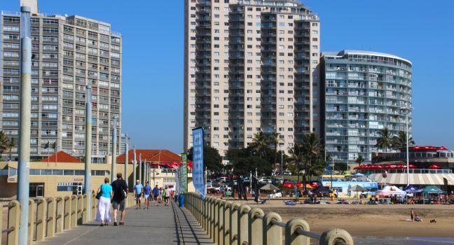DURBAN; SOUTH AFRICA - MAY 3; 2014: People walk along concrete pier towards commercial and residential buildings on beachfront in Durban South Africa;