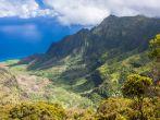 Wide angle panoramic view of the Kalalau Valley on the Na Pali Coast of Kauai, Hawaii. Taken from the Pu'u O Kila Lookout. Photo has white billowy clouds and a deep blue ocean in the background. Landscape shot, green foliage in foreground. cliffs in partia
