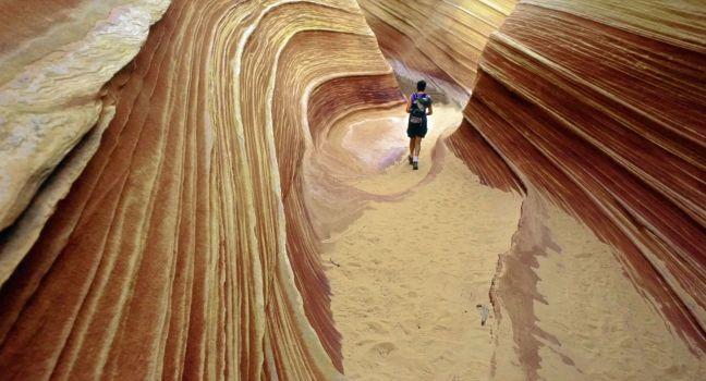 A lone hiker explores the astonishing candy stiped sandstone hidden amongst the geologic folds of the Colorado Plateau, Paria, Arizona