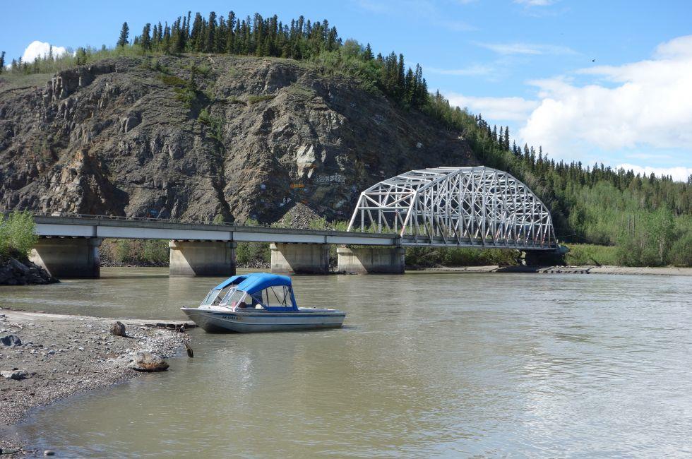 A scenic picture of a bridge in alaska with a small boat on a river.