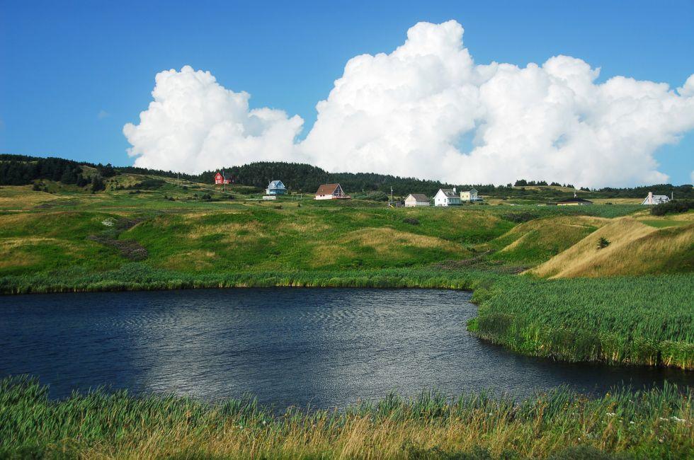A small pond with rolling hills and a big, puffy, cloud in the backdrop. Magdalen Islands.