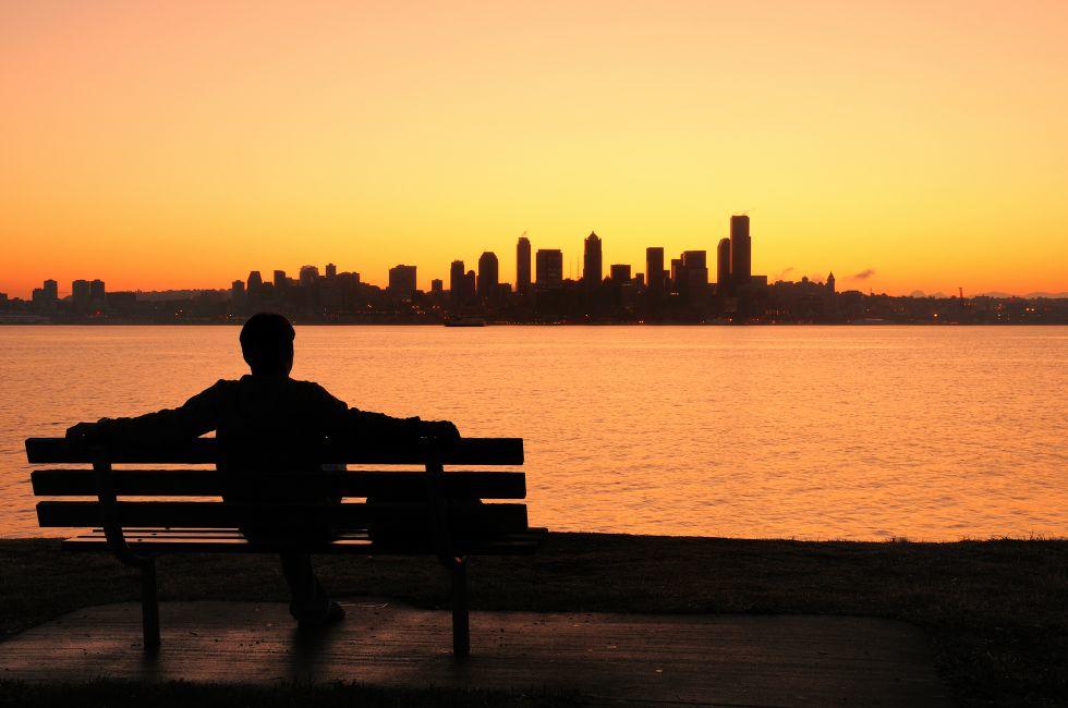 silhouette of a man sitting on a park bench watching the sun rise behind Seattle skyline.