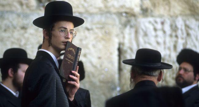 Clutching a siddur prayer book and sporting payos sidelocks, a Jew gathers at the Wiiling Wall where solemn prayers are scribbed and stuffed into the seams of the stone. Jerusalem, Isreal